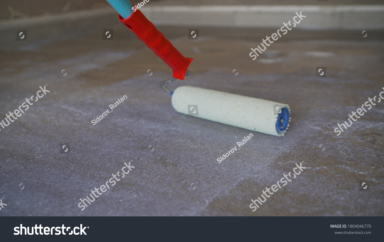 A worker applies the primer to the concrete floor with a roller. Applying a primer to the floor. Floor priming. worker brush primer grout of stones #1804046770