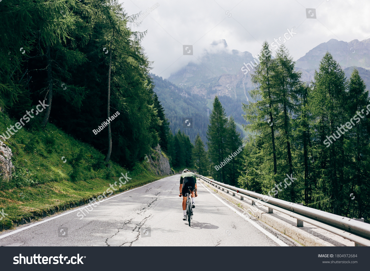 Professional road cyclist on fast and light carbon bicycle descends mountain road in Alps Dolomites. Fit and athletic man on recreational ride trip or training camp, enjoy time outdoors on bike #1804972684