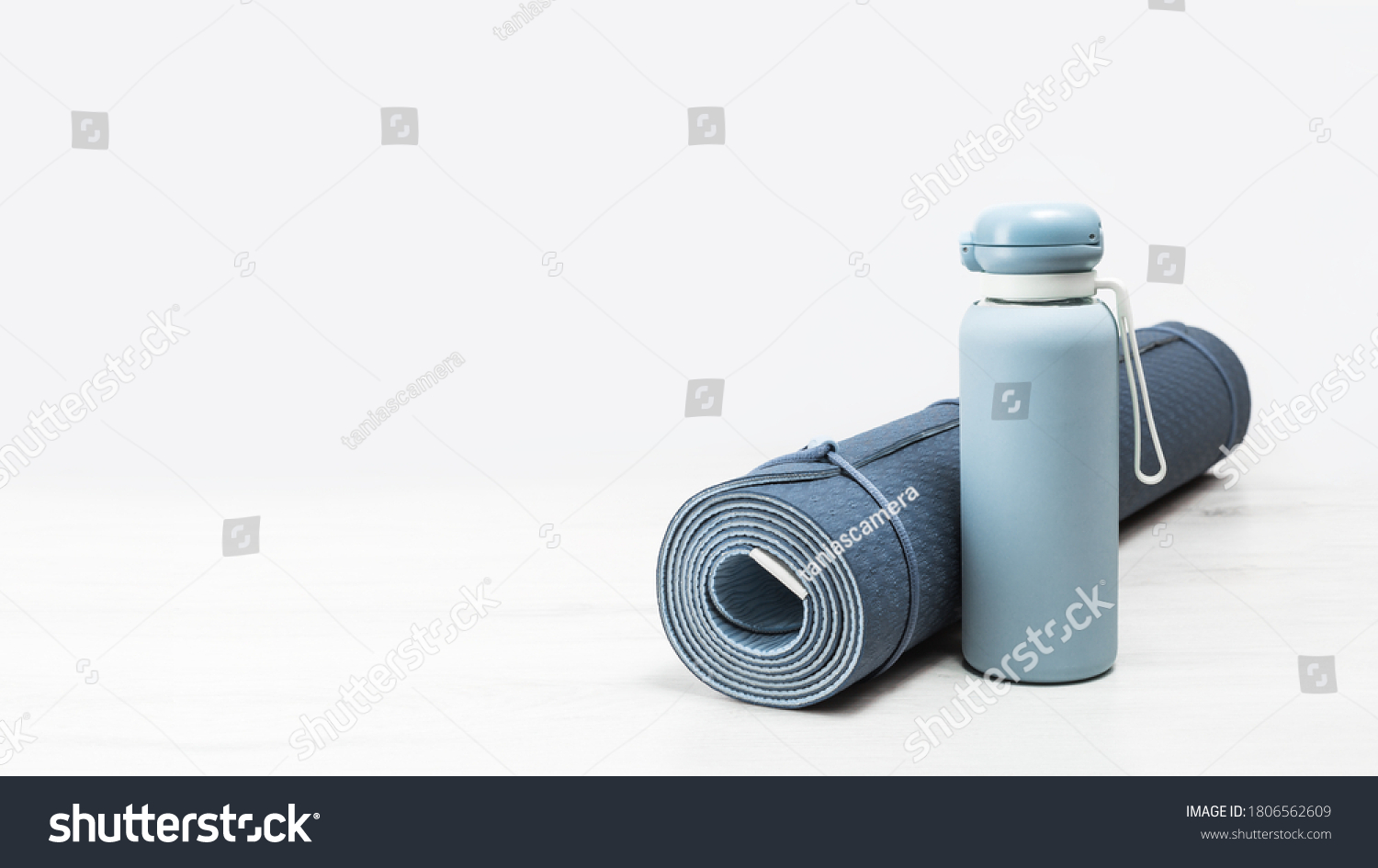 Rolled blue yoga mat and blue water bottle on grey wooden surface. Gender neutral fitness yoga and exercise concept with copy space. Active lifestyle. Workout at home or gym banner #1806562609