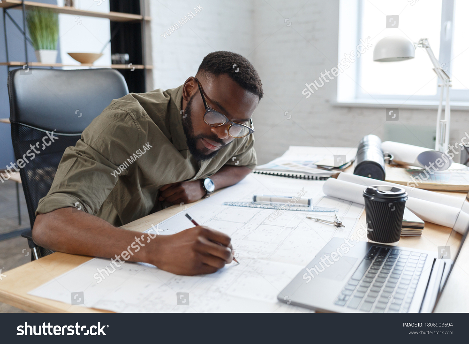 Afro-American architect working in office with blueprints.Engineer inspect architectural plan, sketching a construction project. Portrait of black handsome man sitting at workplace. Business concept. #1806903694