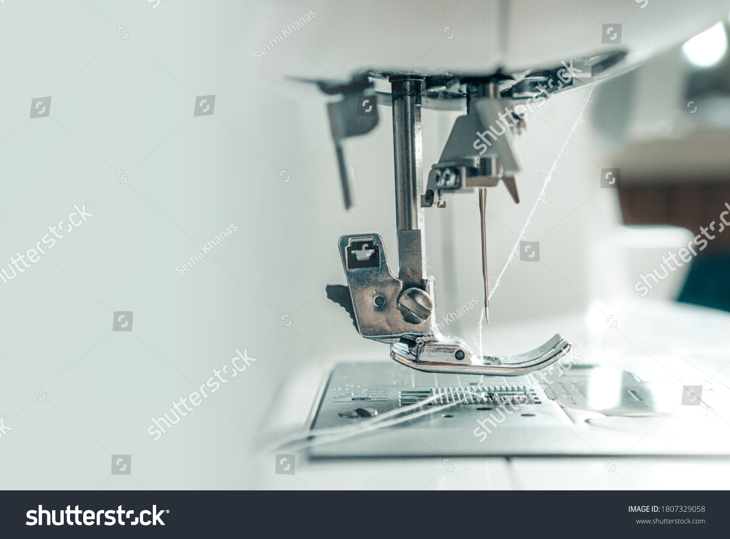 Mechanism of a sewing machine close up. White sewing machine needle with thread with copy space for text. The concept of the garment industry, technology. Photo for garment production. #1807329058