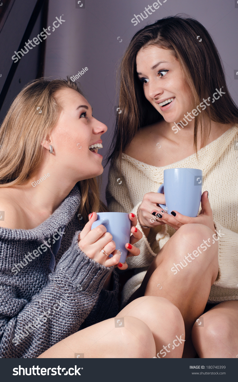 portrait of two young adorable attractive positive women in sweaters smiling and drinking beverages on gray background #180740399