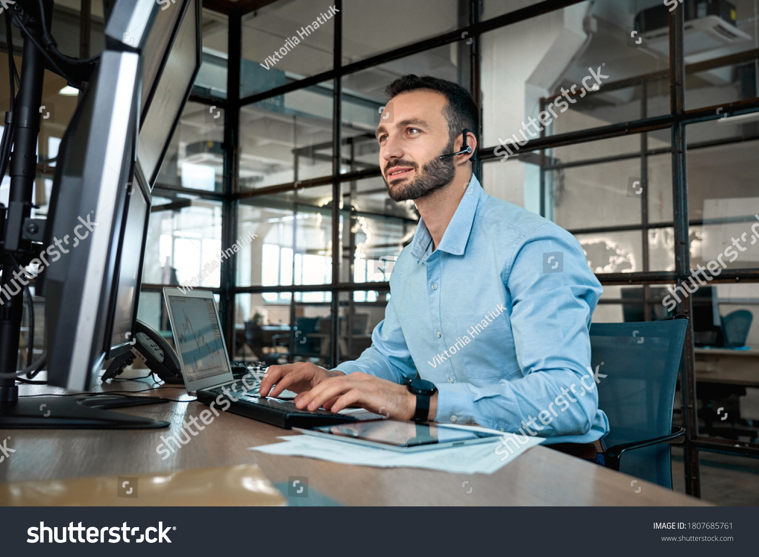Confident stock broker wearing in headset looking at display, analyzing index on crypto currency market diagram, working in office, talking with client #1807685761