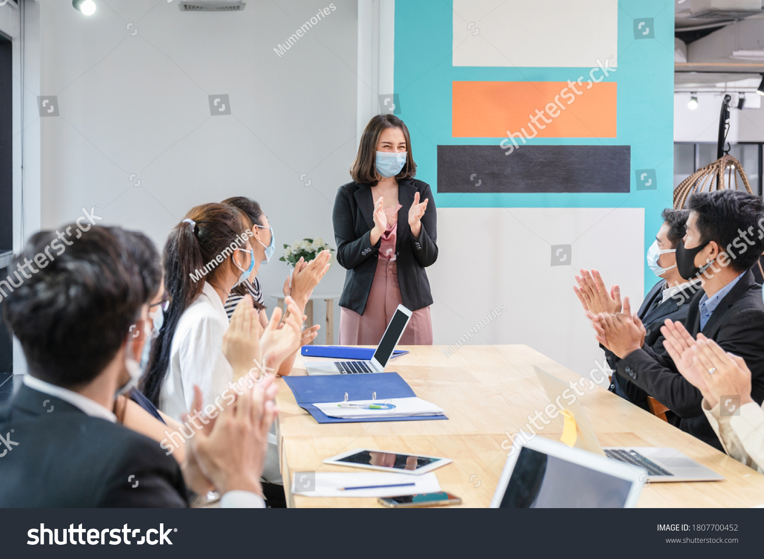 Multi ethnic colleagues celebrating with applauding the female executive while meeting in new normal office. Business team wearing face mask while pandemic of Coronavirus, Covid-19 #1807700452