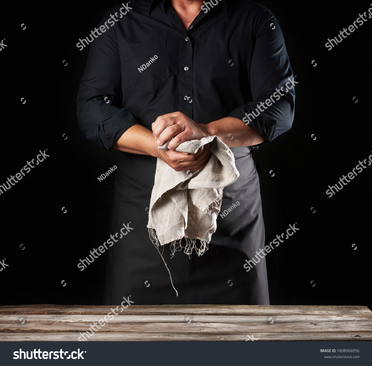 Man in black uniform holds gray linen rag and wipes his hands, chef stands on black background, close up #1808906956