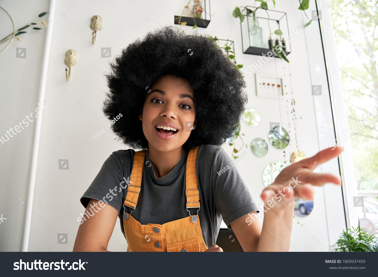 Young African American hipster woman with Afro hair looking at webcam talking to camera with friend online sitting at cafe table making video call, virtual chat, recording blog, headshot portrait. #1809937459