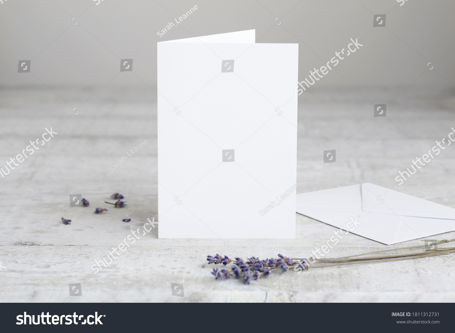 One white greeting card mockup, standing upright on a white wooden desk. Blank, closed card template with envelope.  #1811312731