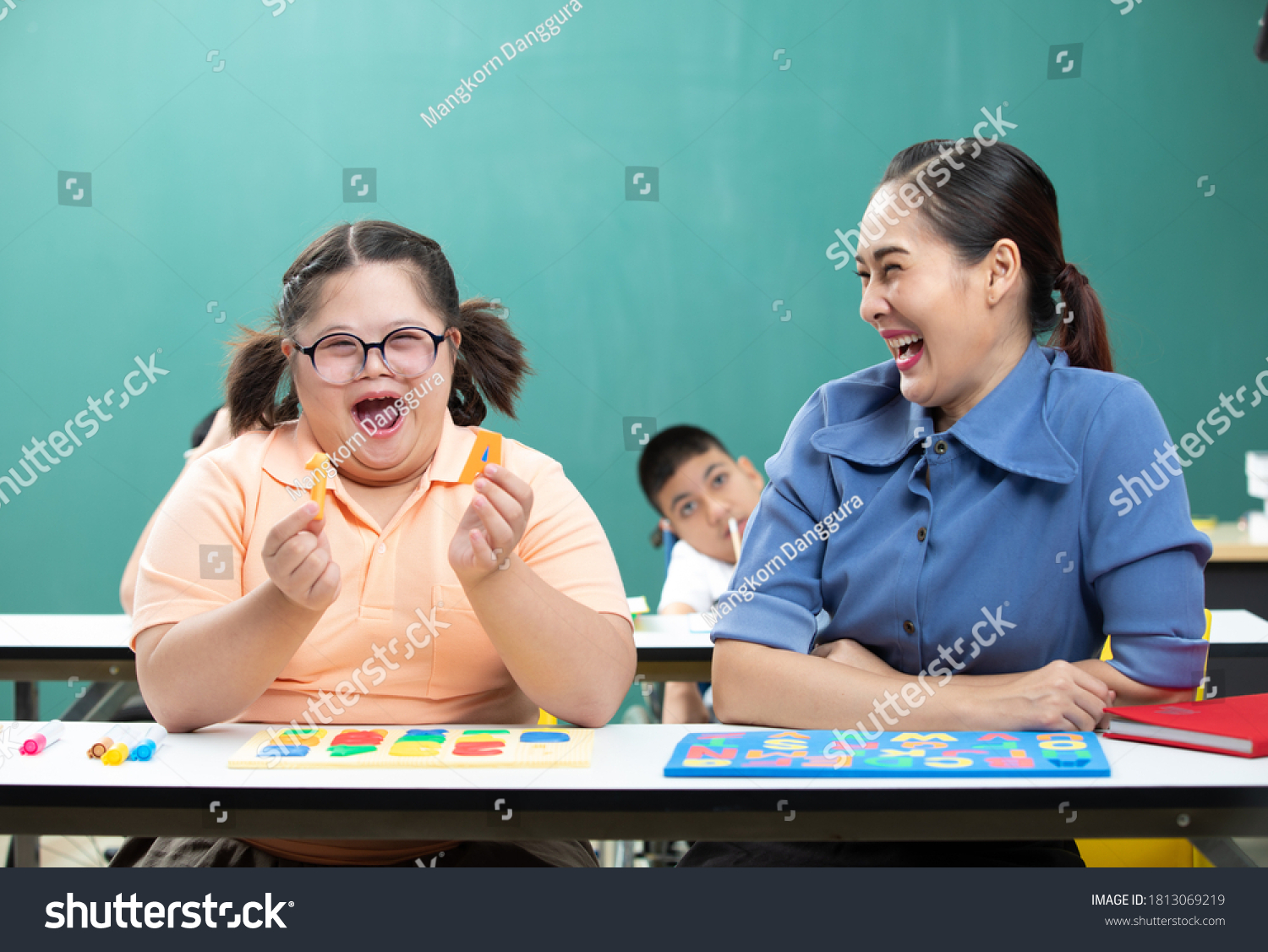 portrait asian disabled child or down syndrome child showing alphabet toy puzzle and woman teacher helping in classroom #1813069219