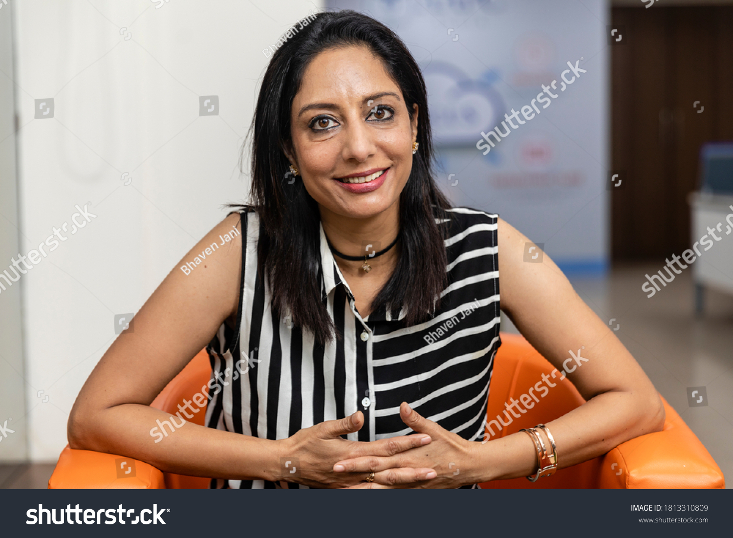 Portrait of smiling Indian business woman sitting on a couch and looking into camera, Corporate environment, smiling face. #1813310809