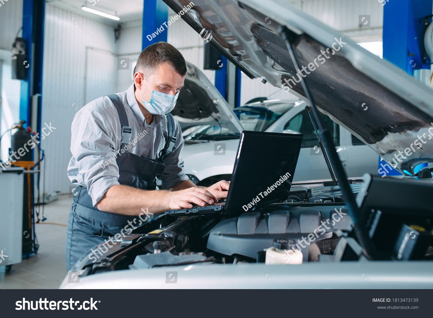 car mechanic using a computer laptop to diagnosing and checking up on car engines parts for fixing and repair #1813473139
