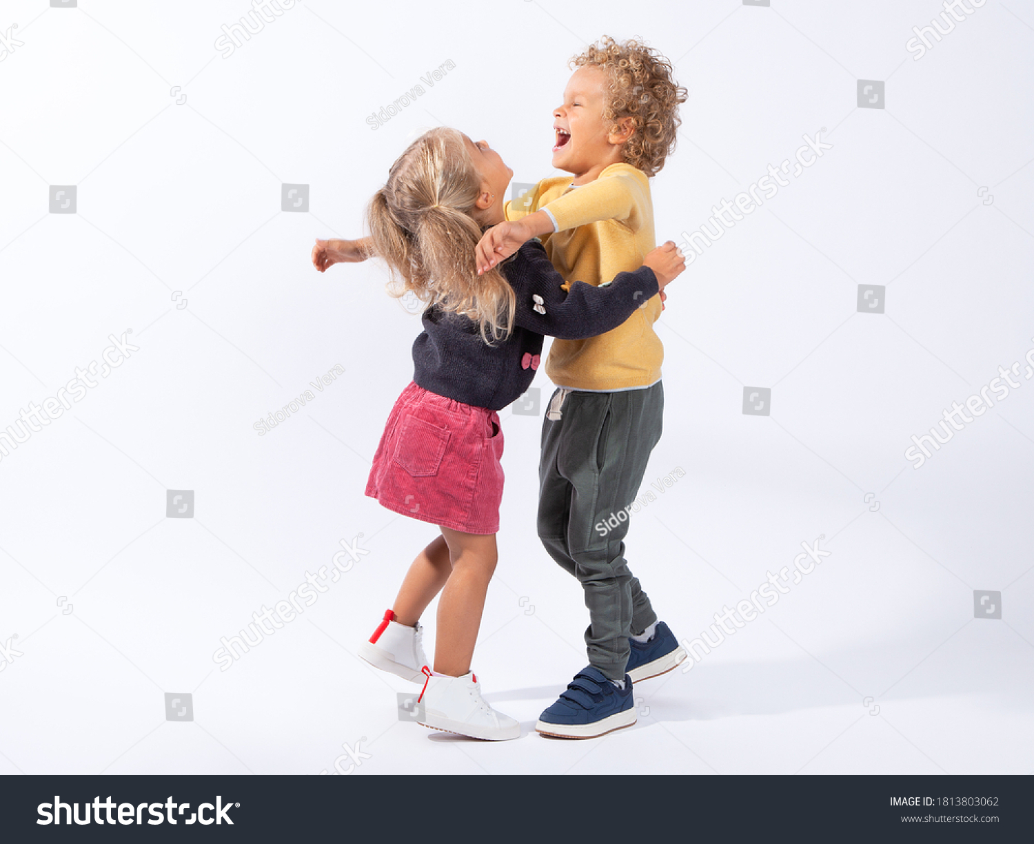 Beautiful European children-brother 4 years old and sister 3 years old on a white background hug, laugh, have fun, indulge. In full growth. The children are tanned and curly-haired. #1813803062
