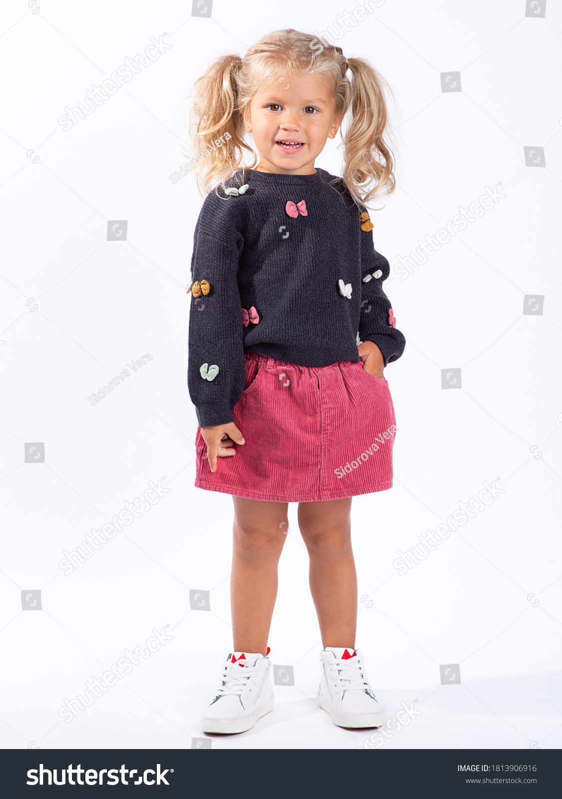 Cute beautiful European blonde girl with two ponytails stands on a white background in full growth. A 3-year-old girl is a model, posing, smiling. #1813906916
