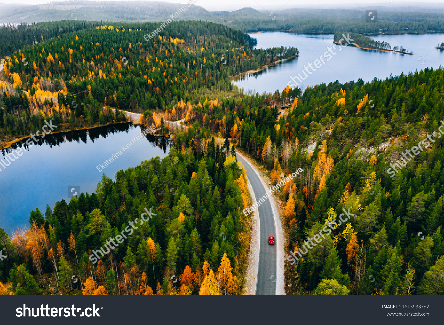 Aerial view of rural road with red car in yellow and orange autumn forest with blue lake in Finland. #1813938752