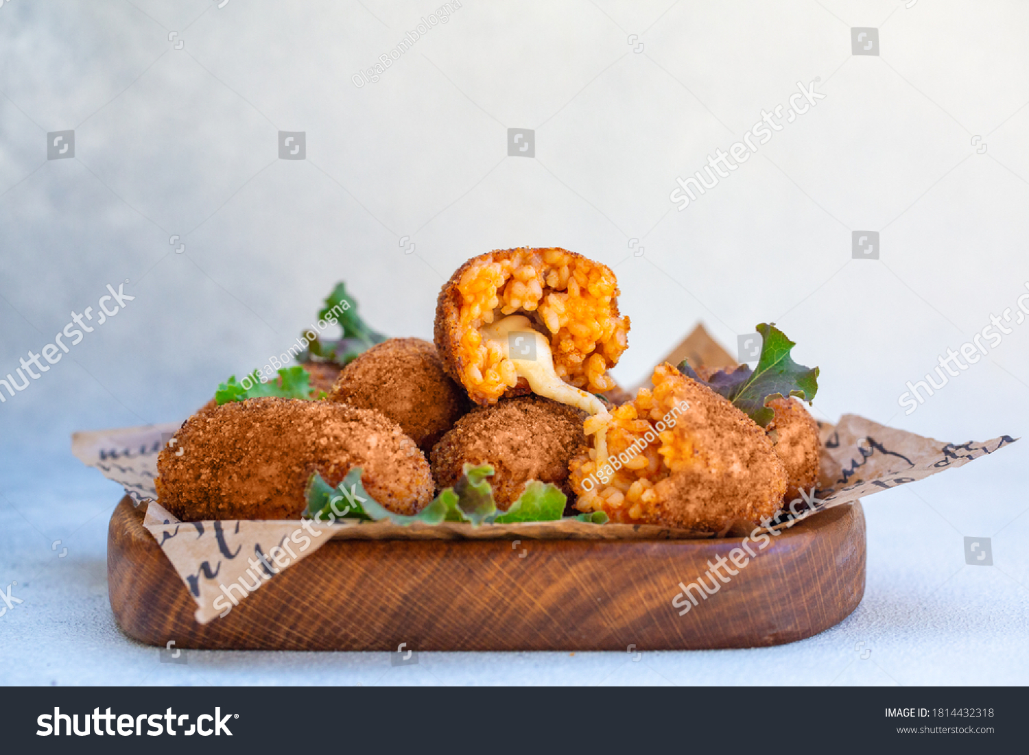 Rice balls stuffed with mozzarella cheese and deep fried on a wooden plate. Light background. #1814432318