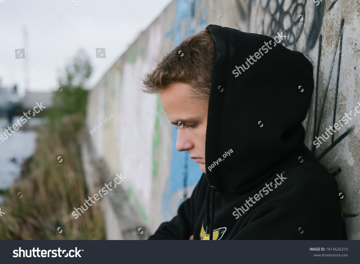 portrait of a sad lonely teenager / young guy in a black hoodie in an abandoned place near the port #1814626310