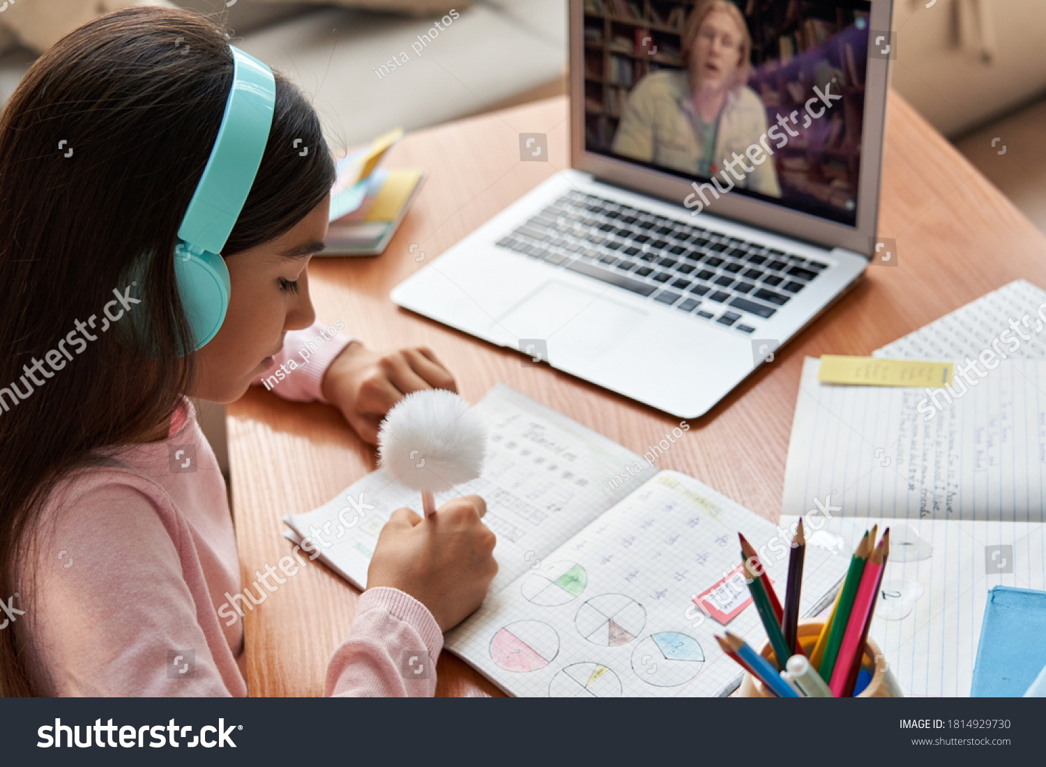 Indian latin preteen girl school pupil wearing headphones distance learning online at virtual lesson with math teacher tutor on laptop screen by video conference call at home. Over shoulder view. #1814929730