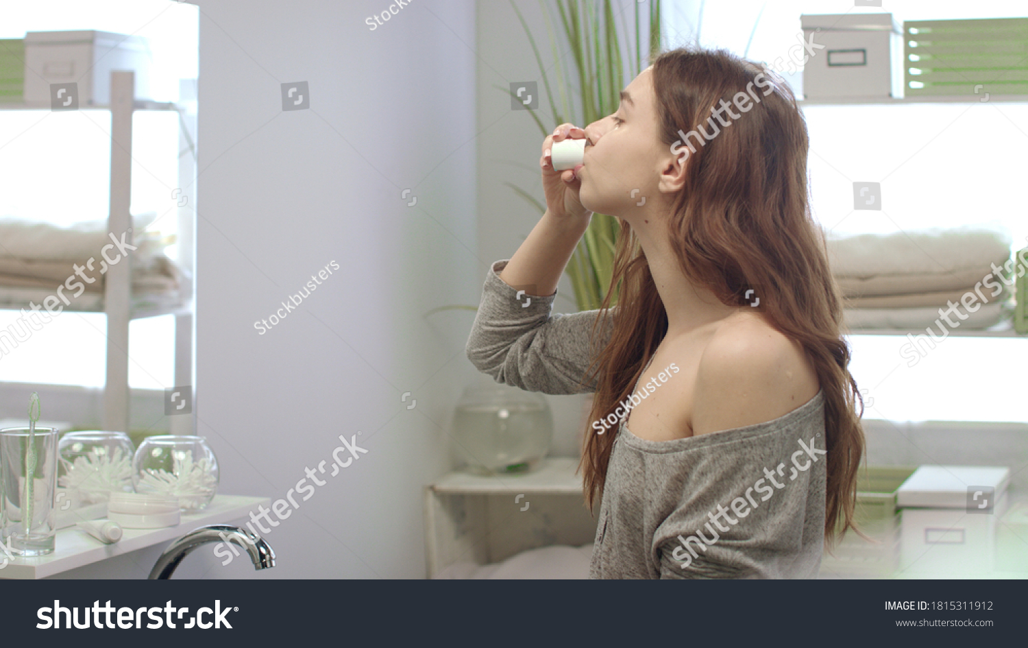 Young woman rinsing mouth with teeth rinse front mirror in bathroom before sleep. Healthy woman using dental rinse while morning care in bath room #1815311912