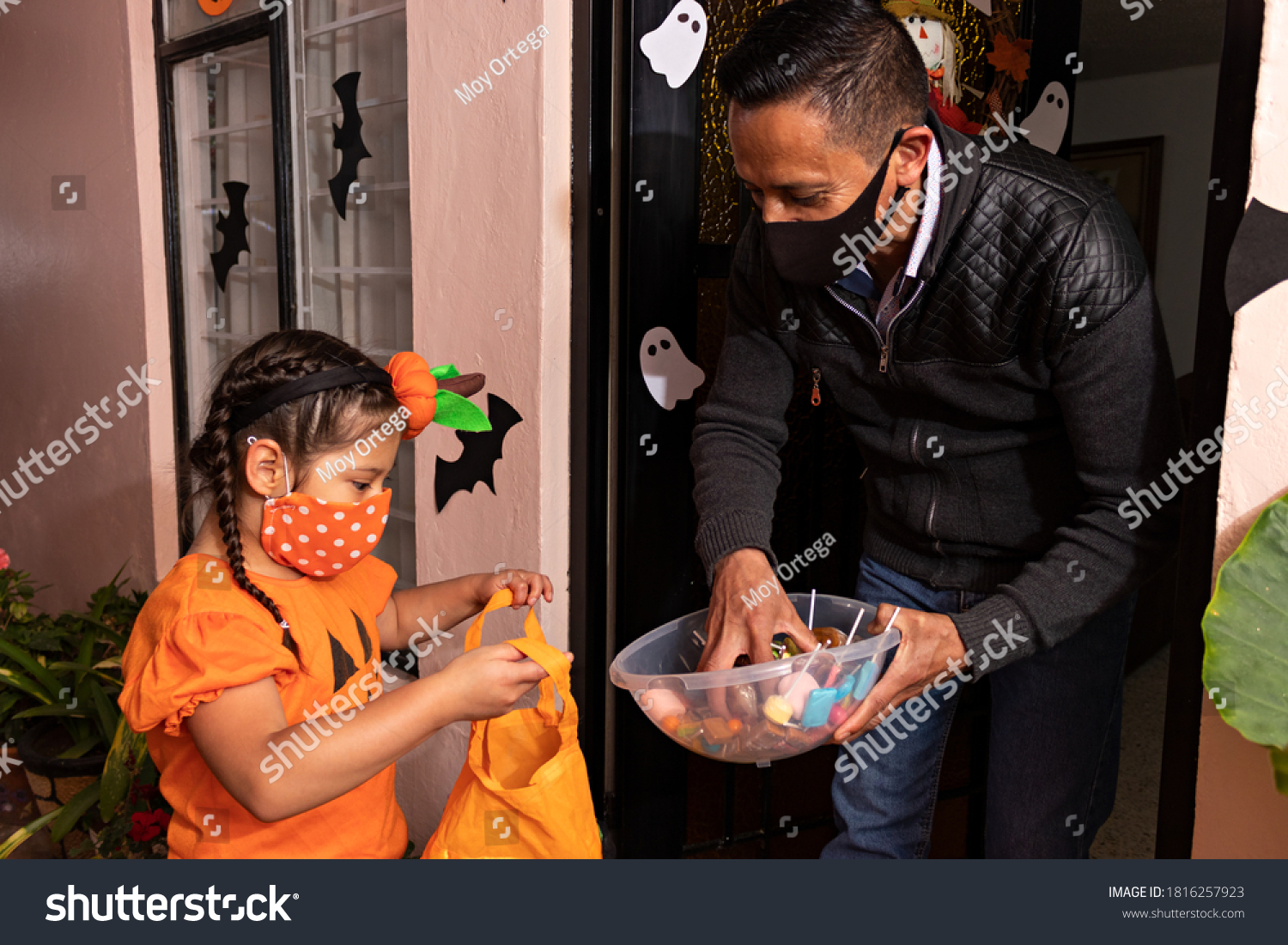A man giving candies to a girl dressed in a pumpkin costume in the night of halloween #1816257923