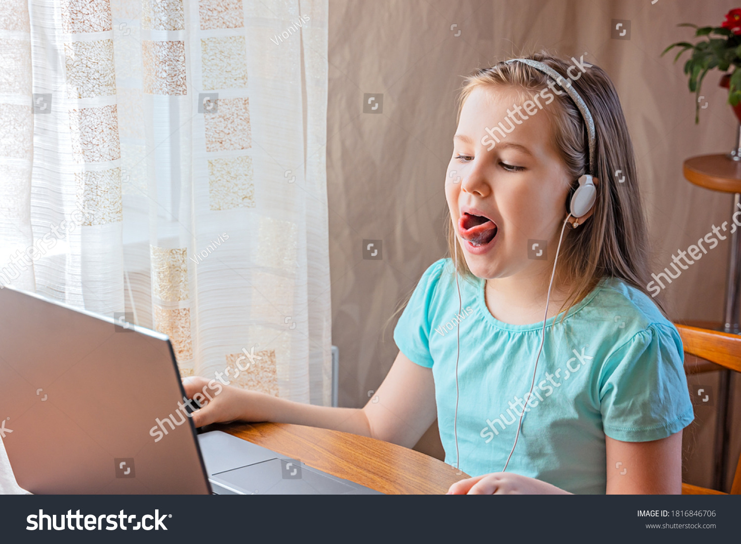 Speech training concept. Little girl uses a laptop to study at home with a teacher, a speech therapist. Distance learning. A kid doing exercises for correct pronunciation. #1816846706