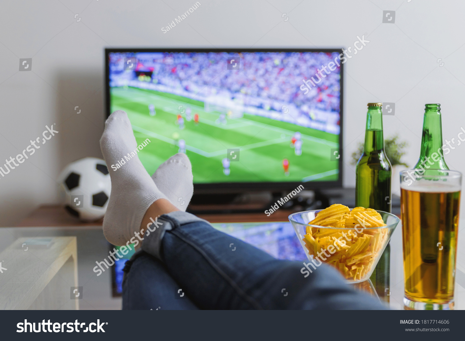 Watching a football match with feet on the table, besides drinks and snacks. #1817714606