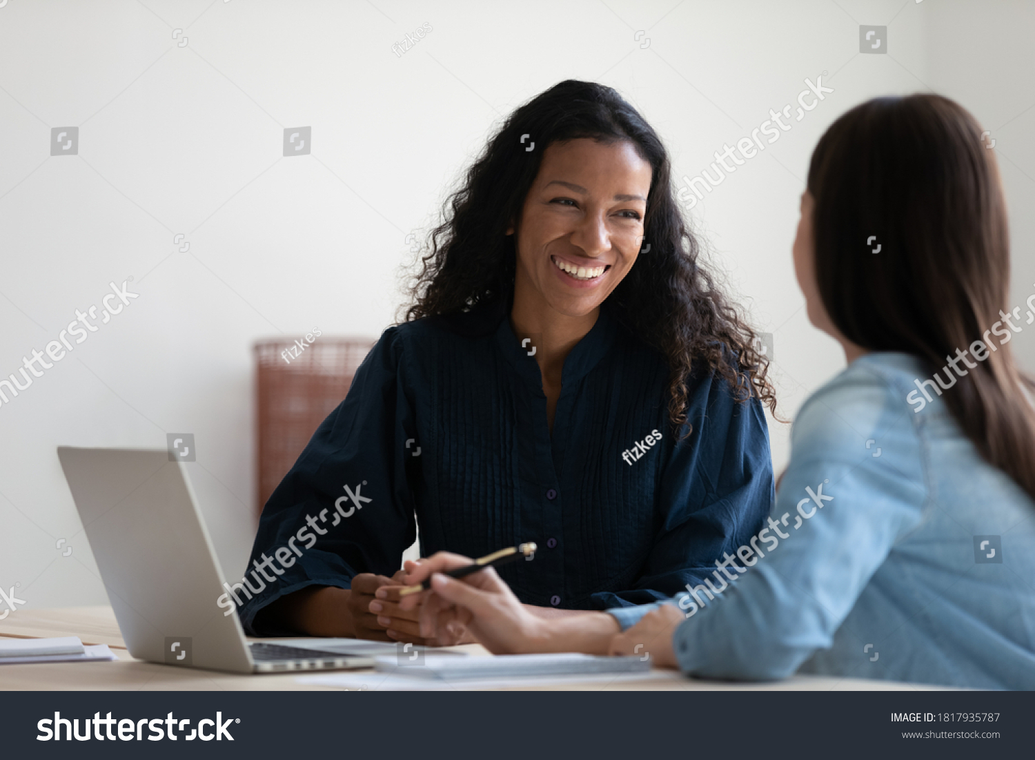 Smiling African American businesswoman talking to colleague, diverse employees brainstorming, sitting at table in office, manager consulting client, using laptop, mentor coach training intern #1817935787
