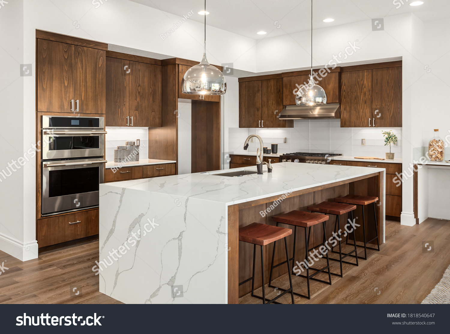 Kitchen in new luxury home with quartz waterfall island, hardwood floors, dark wood cabinets, and stainless steel appliances. #1818540647