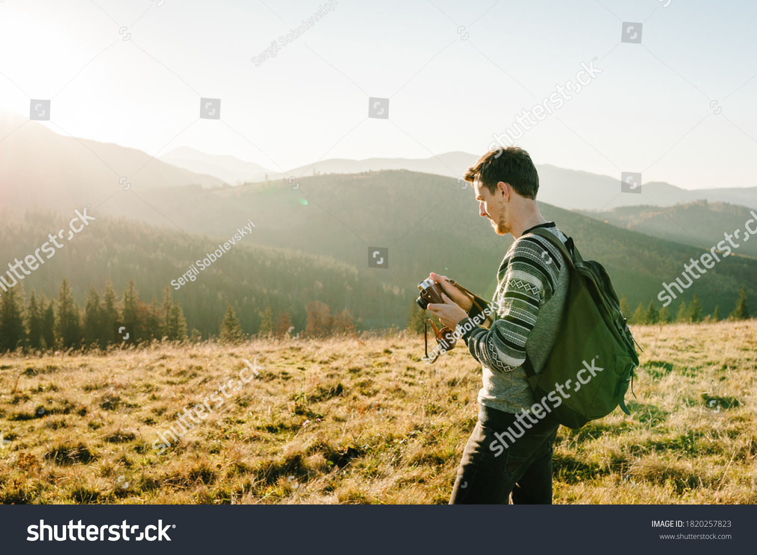 Hiker tourist in the mountains at sunset. Man takes pictures of the sunrise. Hipster with a photo camera and a backpack travels and enjoy nature. #1820257823