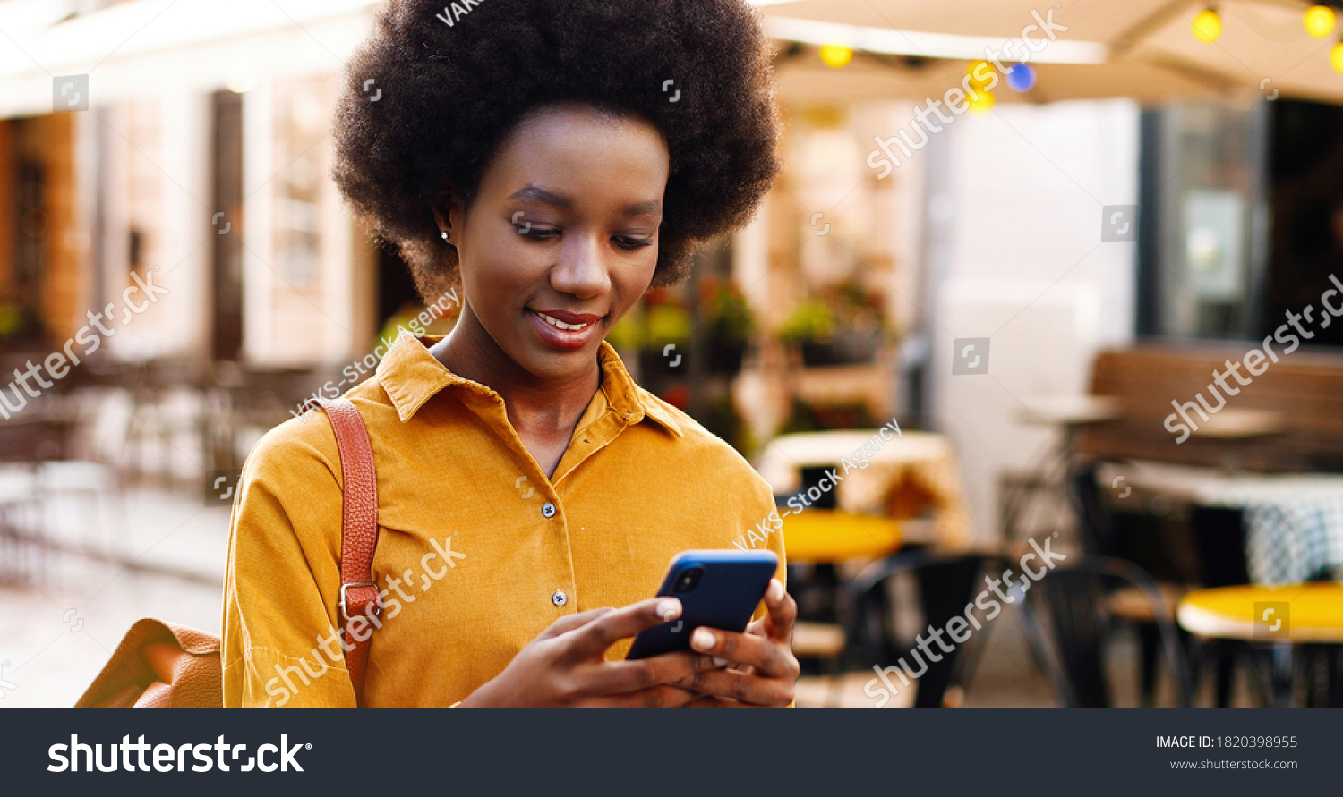 Close up of happy beautiful African American woman texting on smartphone on street. #1820398955