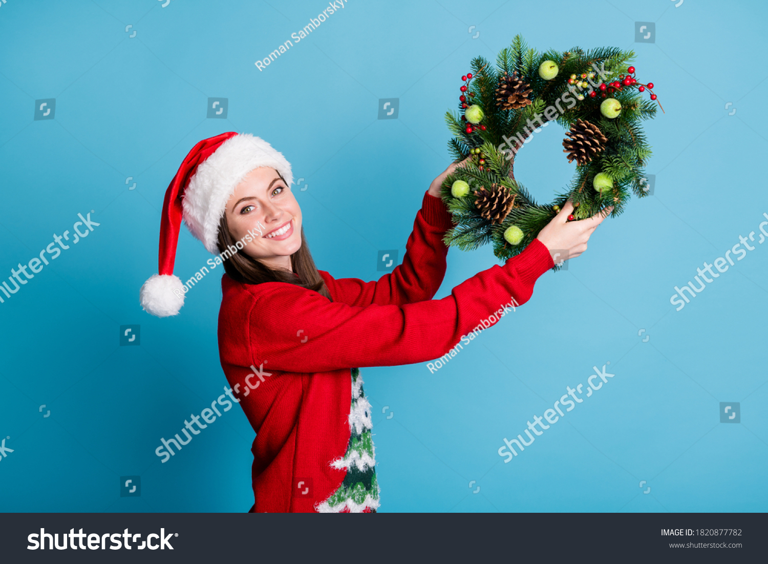 Portrait photo of girl wearing red xmas headwear hanging christmas handmade crafts wreath made of christmas tree branches decorative berries wooden cones isolated on blue color background #1820877782