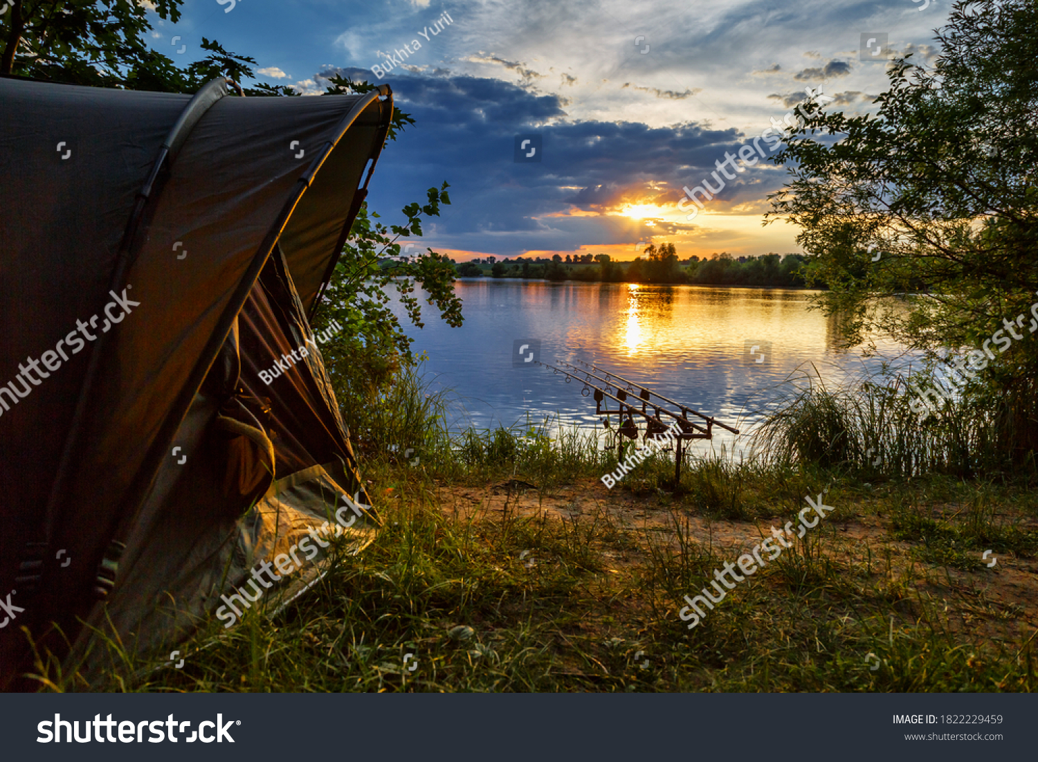 Fishing adventures, carp fishing. Angler, at sunset, is fishing with carpfishing technique. Camping on the shore of the lake.Carp Fishing Sunset #1822229459