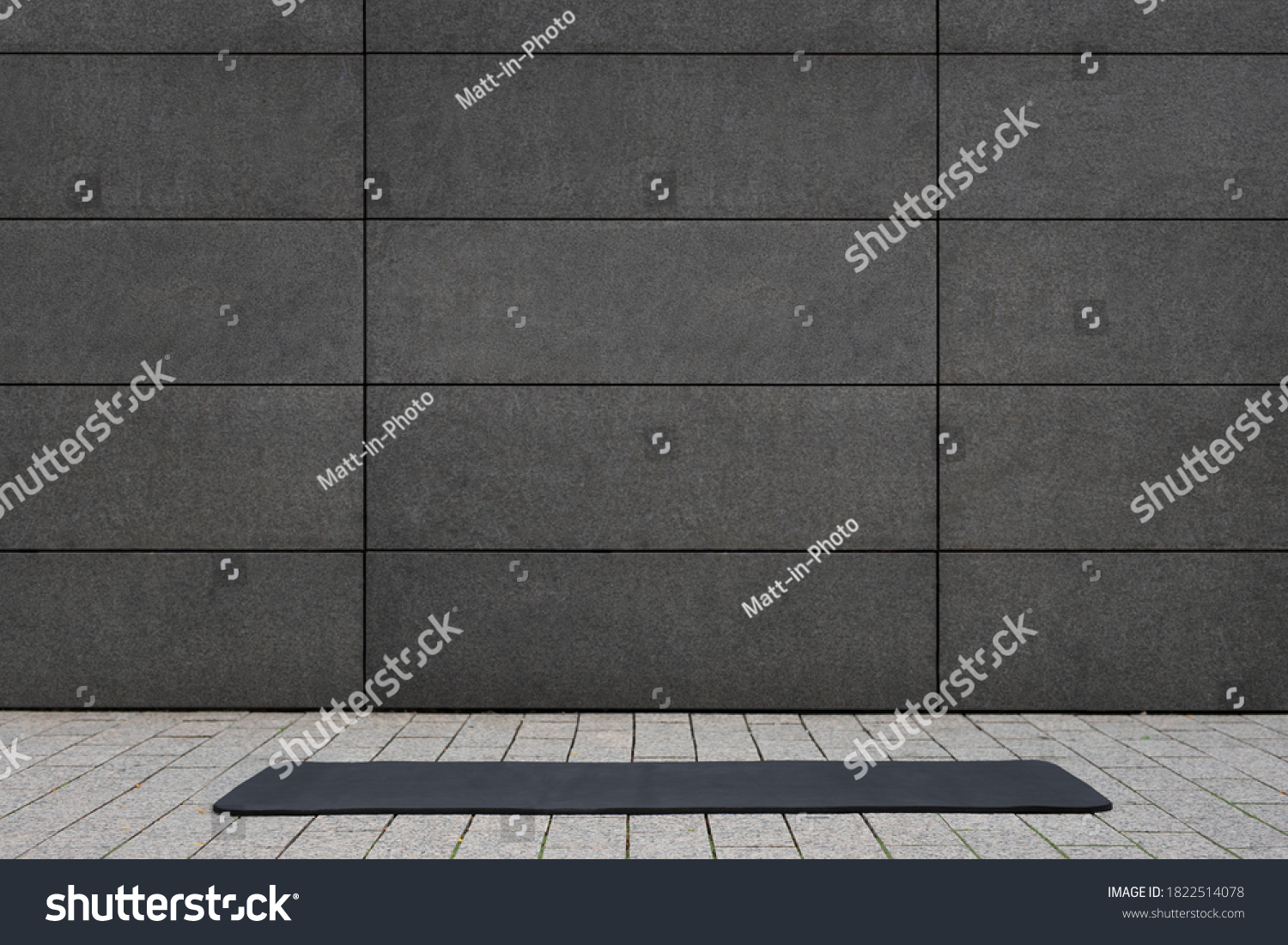 empty and blank foldable black yoga mat on grey sidewalk near empty street outdoor in front of grungy concrete textured wall with copy space is a perfect backdrop for text and yoga fitness graphics #1822514078