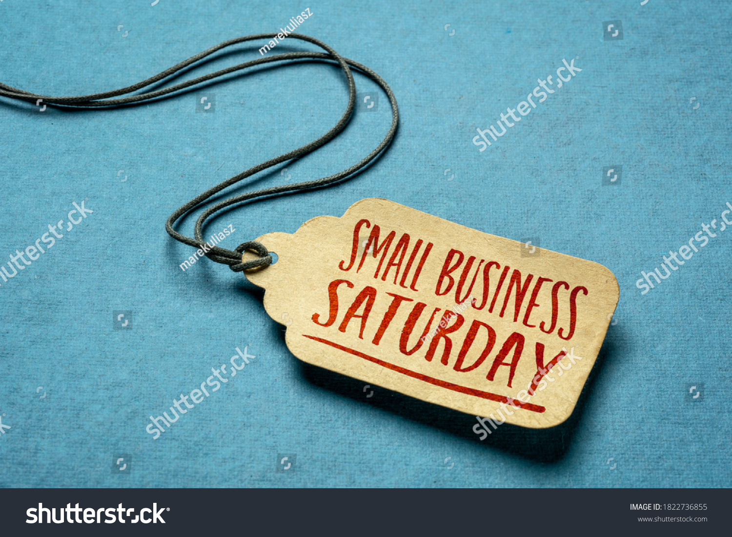 Small Business Saturday sign - a paper price tag with a twine against blue paper background, local holiday shopping concept #1822736855