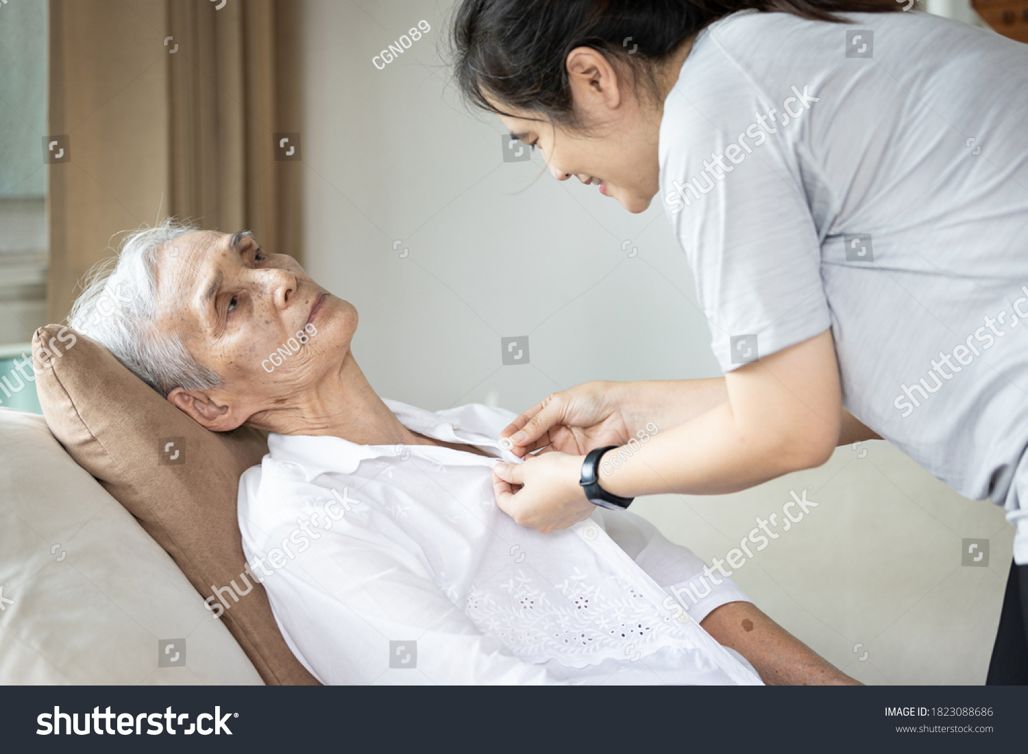 Asian female caregiver taking care of helping elderly patient get dressed,button on the shirt or changing clothes for a paralyzed person,senior woman with paralysis of limbs,body or muscles weakness #1823088686
