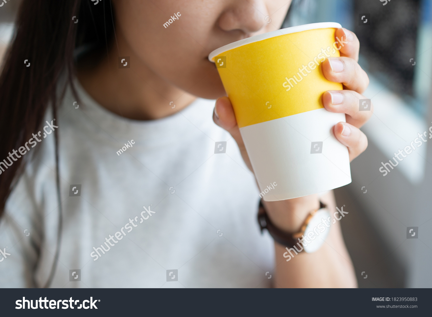 Close up of the Asian lady holding the hot drink paper cup with one hand and sipping the hot beverage #1823950883
