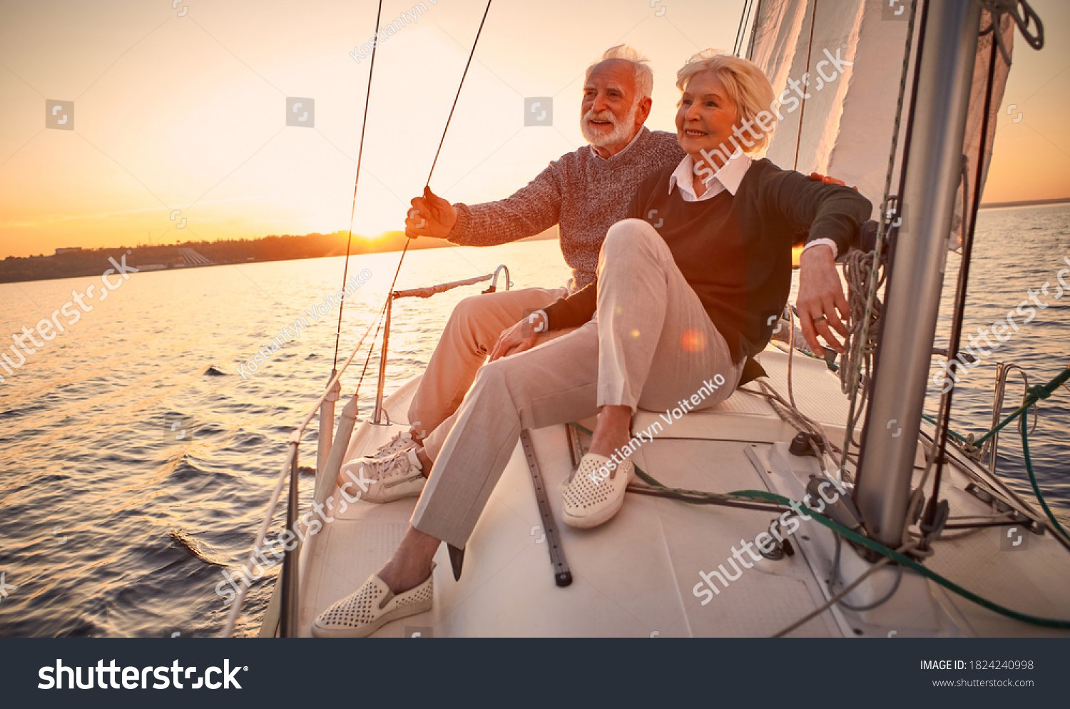 Beautiful and happy senior couple in love sitting on the side of sailboat or yacht deck floating in sea at sunset and enjoying amazing view, sailing together #1824240998