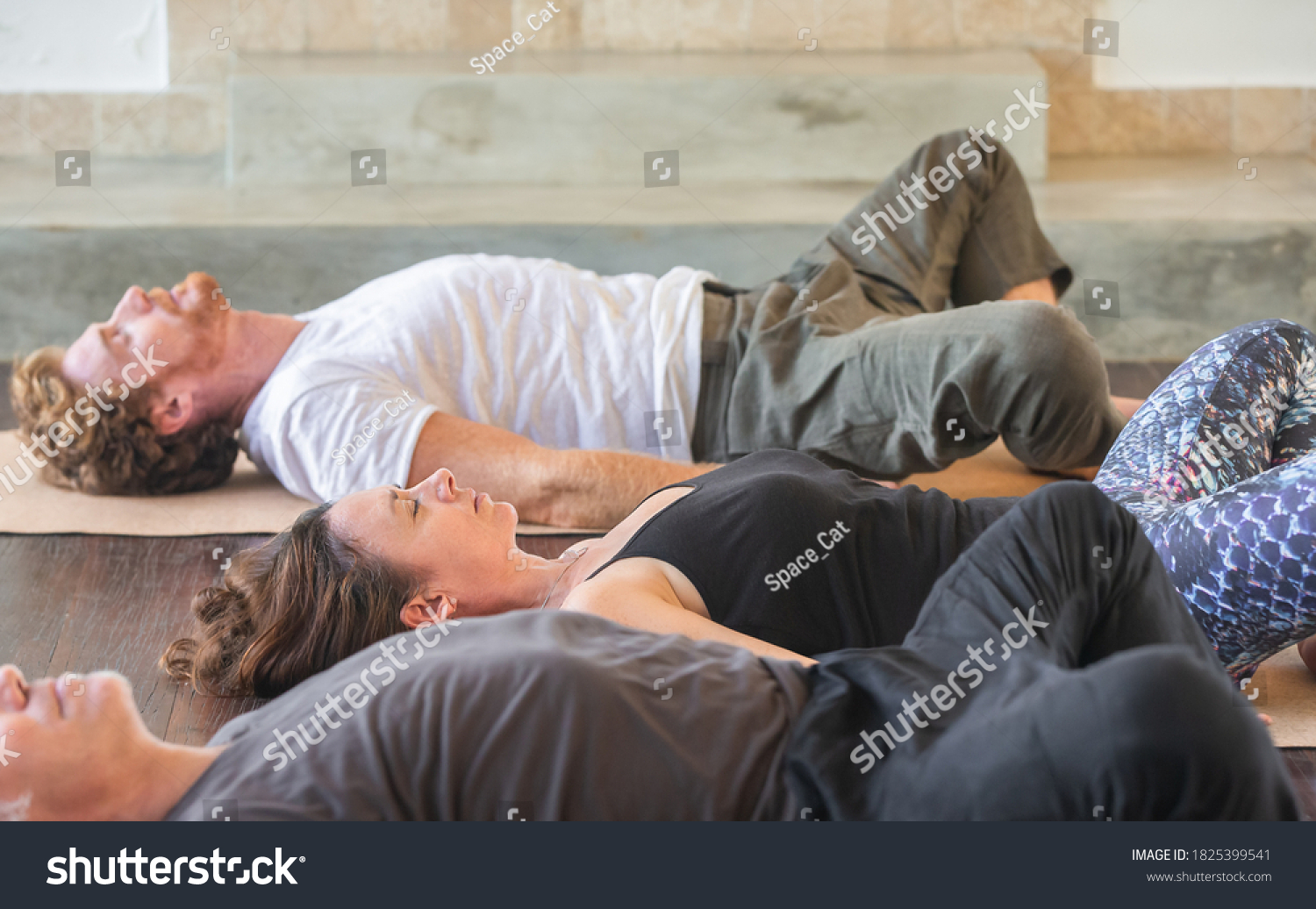 Diverse group of people on wooden floor practicing yoga lying in Reclined Butterfly exercise relaxing after practice. Healthy lifestyle concept #1825399541
