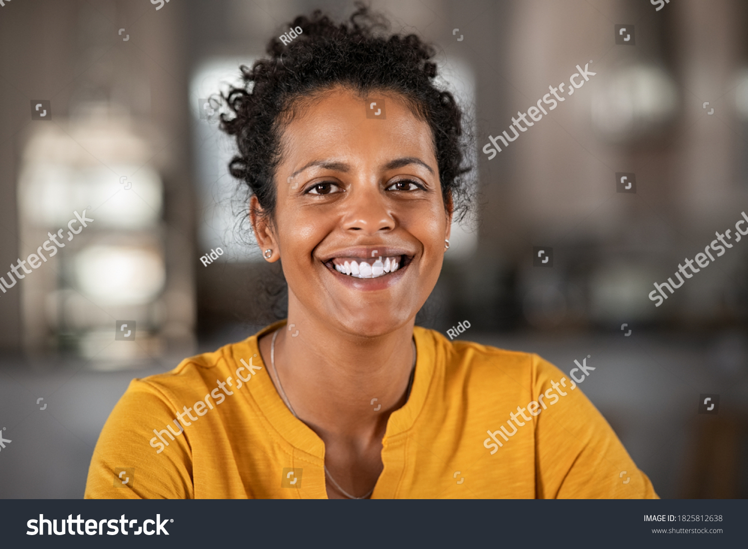 Portrait of a beautiful mid adult woman smiling at home. Middle aged african woman in casual looking at camera with copy space. Cheerful mixed race girl relaxing at home with big laugh. #1825812638