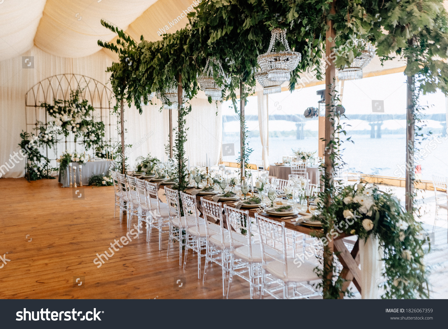 Banquet tables decorated with arrangements of flowers, herbs and candles in the tent. Wedding. Banquet.Crystal chandeliers hang from above #1826067359