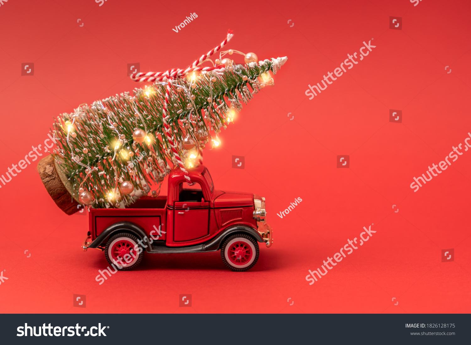 Red small retro toy truck with sparkling Christmas tree lights on truck body on red background. Delivery, christmas, New Year concept. Copy space, selective focus. #1826128175