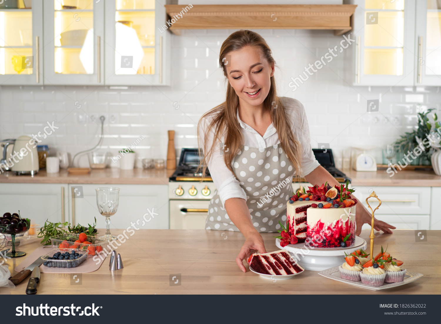 pastry chef in the kitchen makes desserts, cakes and muffins. Cooking at home. Delicious and beautiful homemade cakes, pastry recipes. A young woman in an apron in the kitchen made a red velvet cake #1826362022
