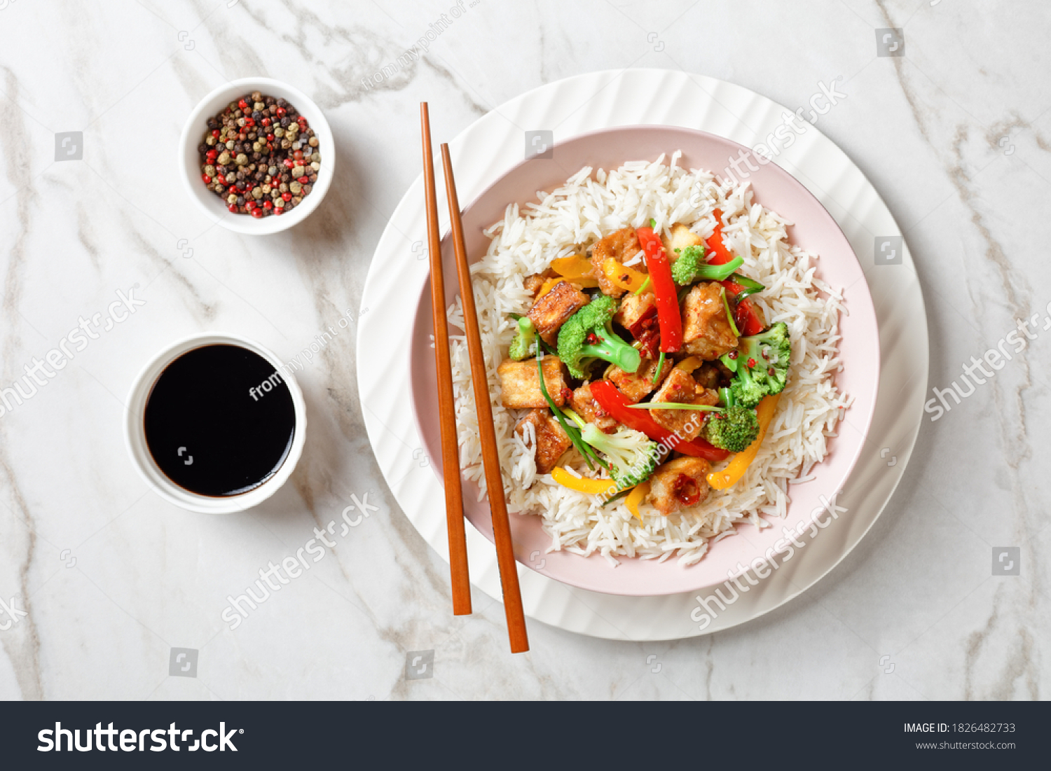 Japanese dish katsu chicken curry with vegetables: broccoli, red and yellow sweet pepper and parsley over jasmine rice served on a pink plate on a stone background served with chopsticks, close-up #1826482733