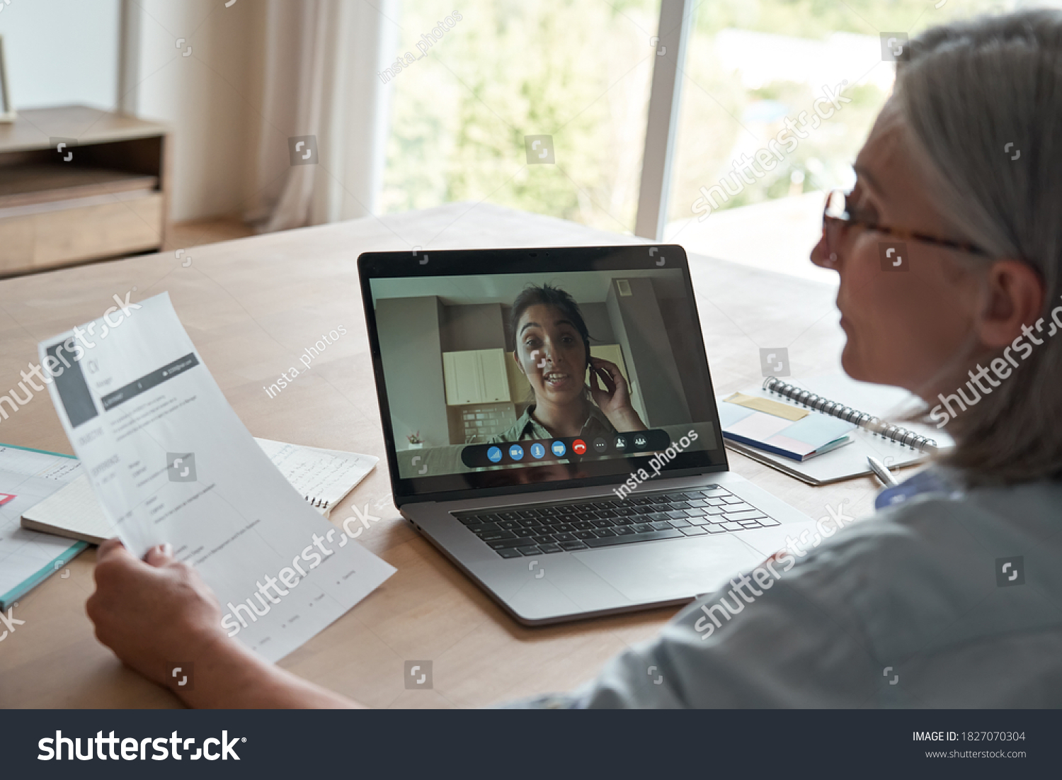 Old female hr reading cv during online job interview by video call. Senior employer checking indian seeker resume talking by social distance remote recruitment chat meeting videoconference on laptop. #1827070304