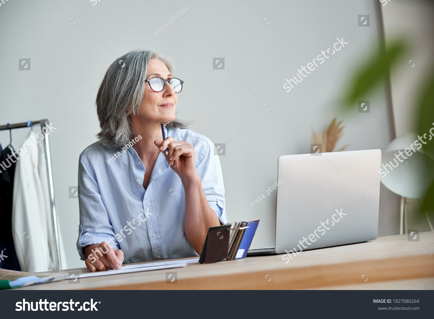 Inspired mature grey-haired woman fashion designer thinking on new creative ideas at workplace. Smiling beautiful elegant classy middle aged older lady small business owner dreaming in atelier studio. #1827080264