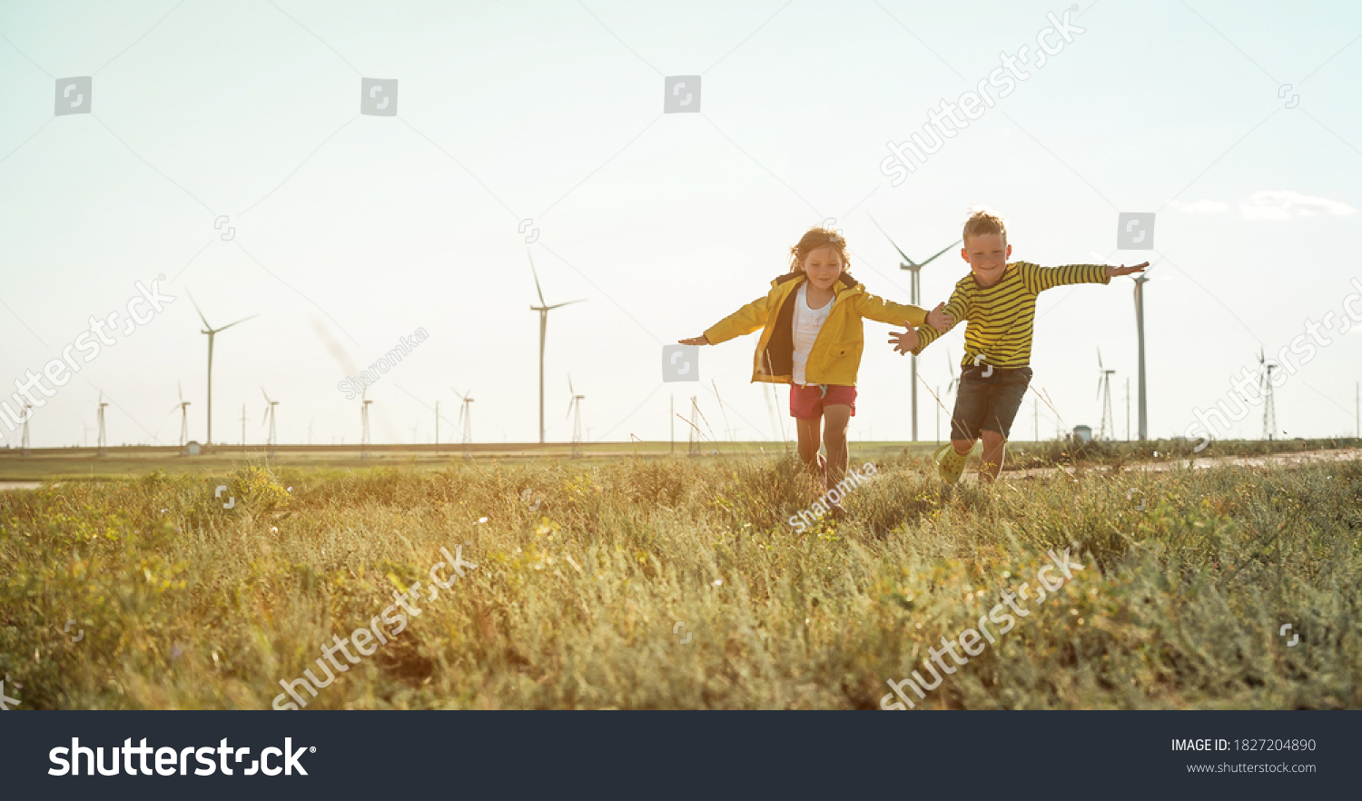 Little girl and boy are running in front of windmills. Renewable energies and sustainable resources - wind mills. children playing with the wind near a wind turbine #1827204890