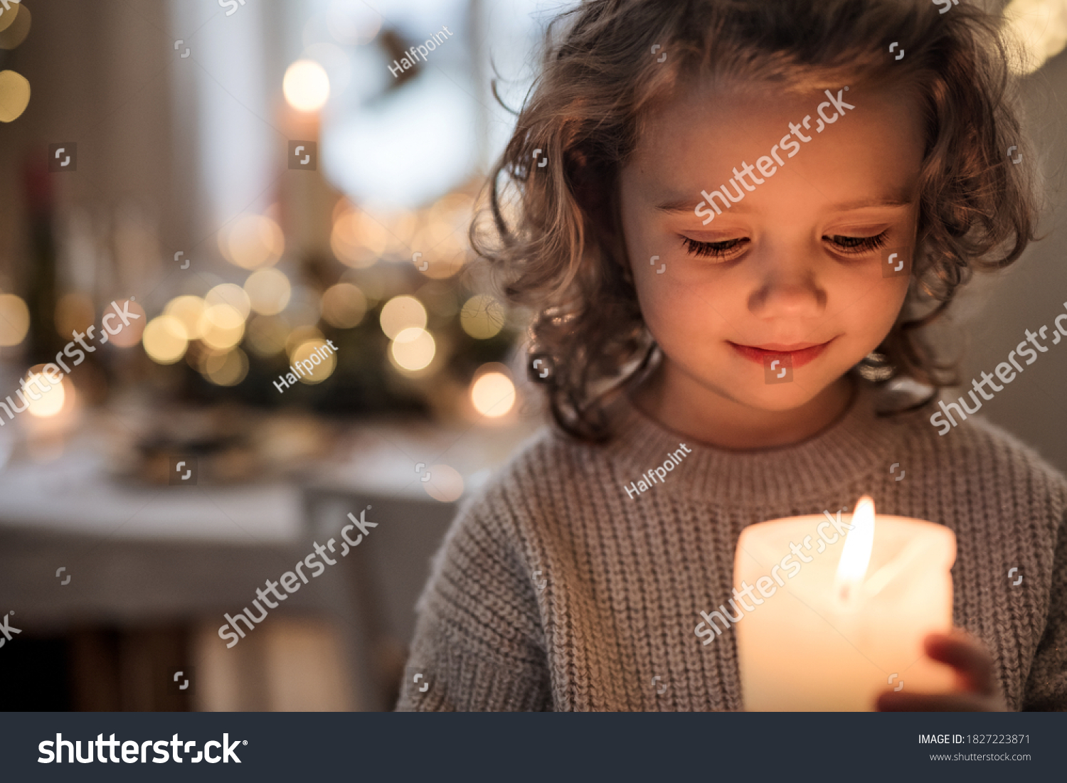 Cheerful small girl indoors at home at Christmas, holding candle. #1827223871