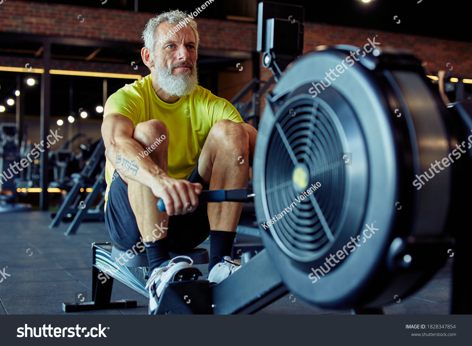 Sport and fitness after 50. Strong mature athletic man in sportswear exercising on rowing machine at gym #1828347854