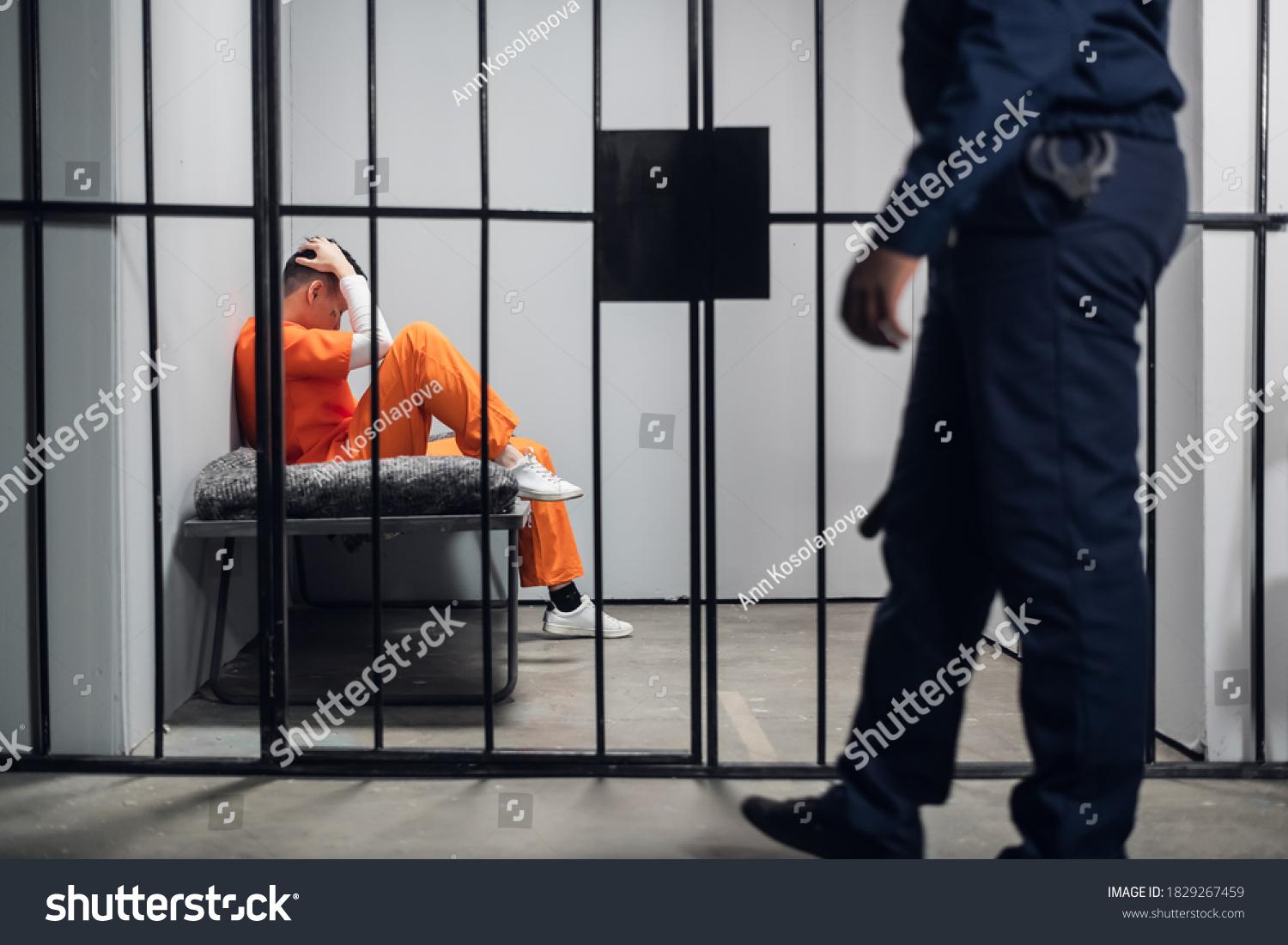 A prison guard makes a tour of the cells in a high-security prison. The cells are occupied by criminals in red robes #1829267459