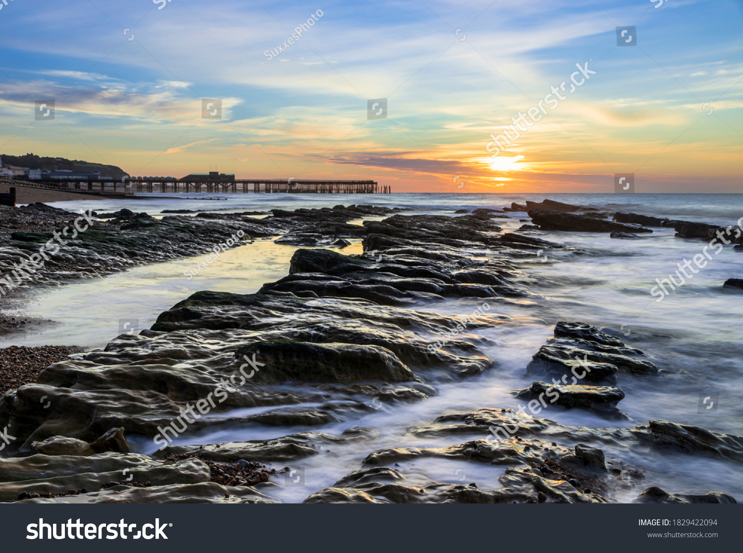 The sun rising and the tide receding revealing the rocks on St Leonards beach with Hastings pier on the horizon, east Sussex south east England #1829422094