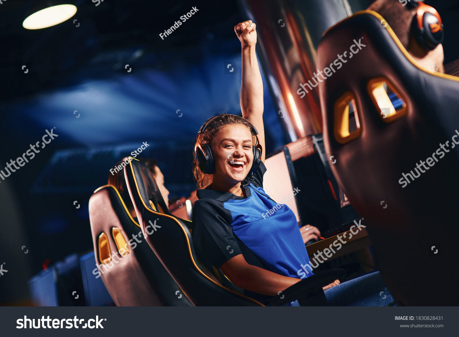 Young happy mixed race girl, female cybersport gamer raising hand up and smiling at camera while participating in eSport tournament #1830828431