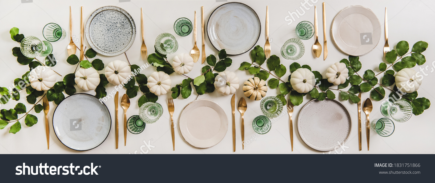Fall table setting for celebration Thanksgiving or Friendsgiving day, family party or gathering. Flat-lay of plates, cutlery, glassware, pumpkins and leaves over plain white table background, top view #1831751866